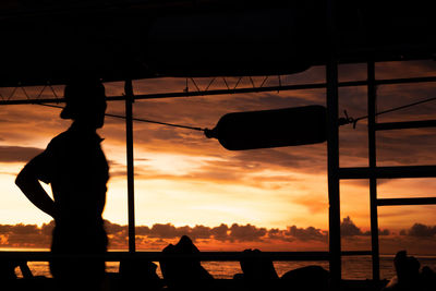 Silhouette people standing by sea against sky during sunset