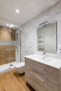 Simple and modern bathroom with marble white tiles, wooden finishing, toilet and shower