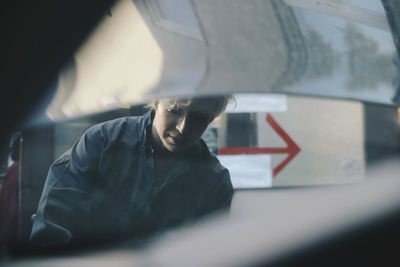 Female mechanic seen through open car hood