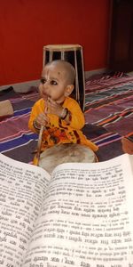 Boy sitting with stick on floor with book at home