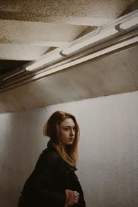 Portrait of beautiful young woman standing against wall