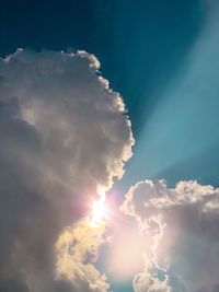 Low angle view of sunlight streaming through clouds