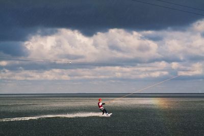 Man waterskiing in sea against cloudy sky