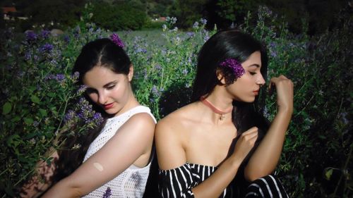 Beautiful young female friends sitting by flower plants on field