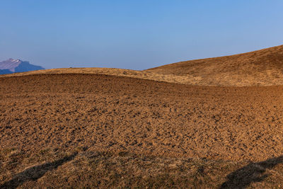 Plowed red earth fields on the background of the blue sky with a shadow in the foreground