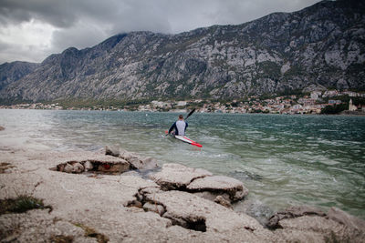 Man kayaking in river against mountains