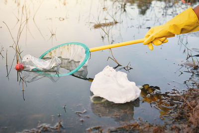 Cropped hand of boy removing bottle from net floating in lake