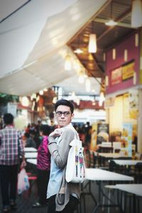 Thoughtful man with bag standing at sidewalk cafe in city