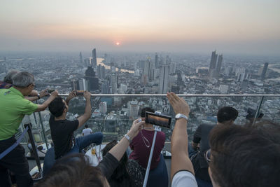 Group of people photographing cityscape against sky during sunset