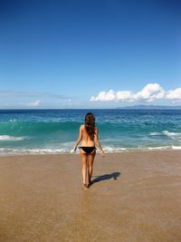 Full length of young woman on beach against blue sky