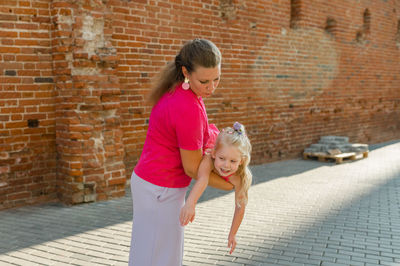 Side view of young woman holding cat while standing against brick wall