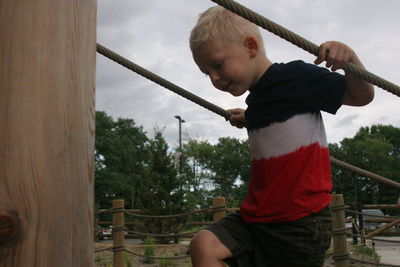 Boy playing on railing against sky