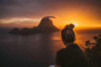 Woman sitting against sea during sunset