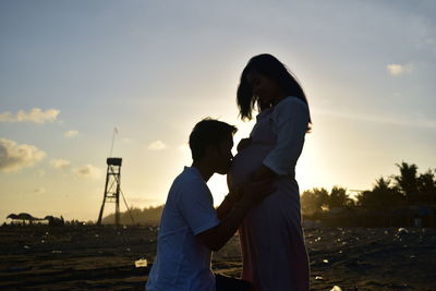 Silhouette man kissing stomach of pregnant woman against sky during sunset