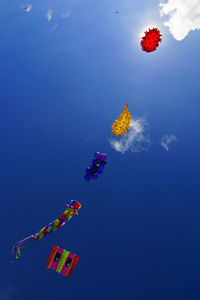 Low angle view of colorful kites flying against blue sky