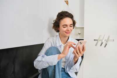 Young woman using mobile phone while standing against wall