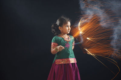 Girl spinning sparkler while standing against black background