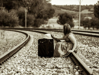 Side view of woman sitting on railroad track