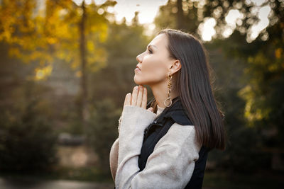 Side view of young woman standing against trees