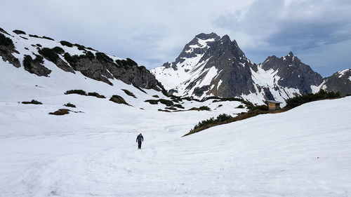Mid distance of man walking on snow covered landscape against snow capped mountain
