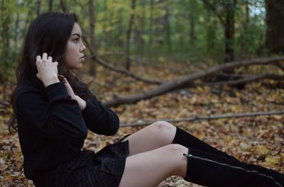 Young woman looking away while sitting on land in forest