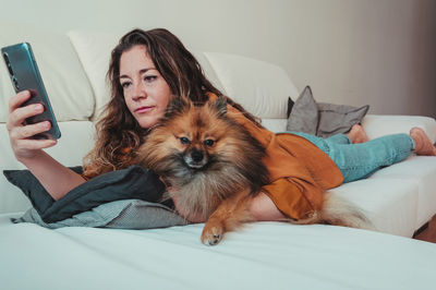 Full length of woman lying down on sofa with dog at home