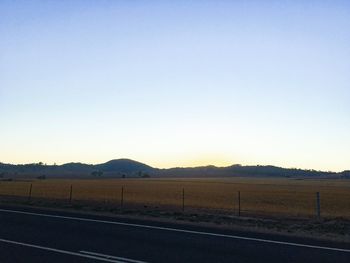 Road by field against clear sky