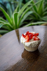 Homemade buttercream cupcakes with fresh strawberries on wooden table.