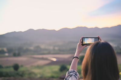 Woman use mobile phone for shoot a photograph of golden hour mountain range