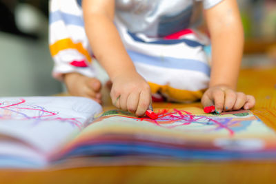 Low section of boy with book on table at home