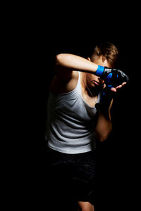 Young man boxing against black background