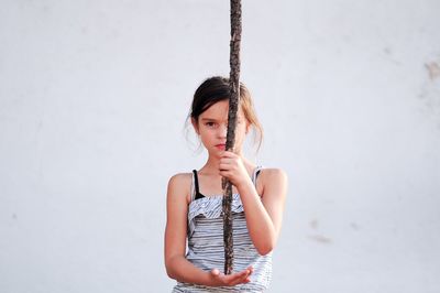 Portrait of girl holding stick while standing against wall