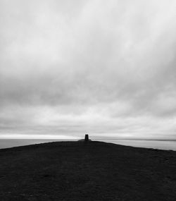 Silhouette person standing on shore by sea against sky