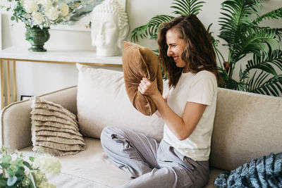 An angry woman screams into a pillow and slams her fists on the couch.