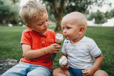 White male siblings sharing ice cream sitting on the grass