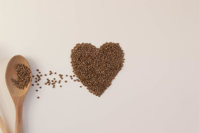 Heart made of raw lentils on a white background with kitchen utensils such as wooden spoon. 