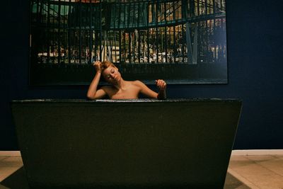 Shirtless young woman sitting in bathtub at bathroom