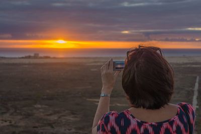 Woman photographing sunset with mobile phone