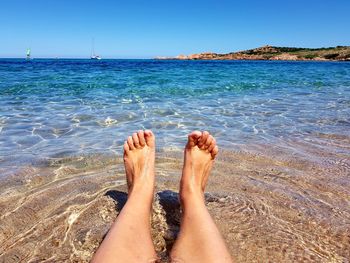 Low section of woman relaxing at sea shore against clear sky