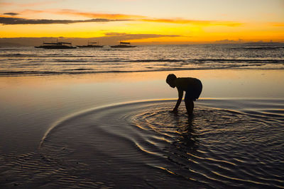 Silhouette man standing on beach against sky during sunset