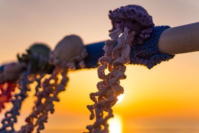 Close-up of hand holding orange against sky during sunset