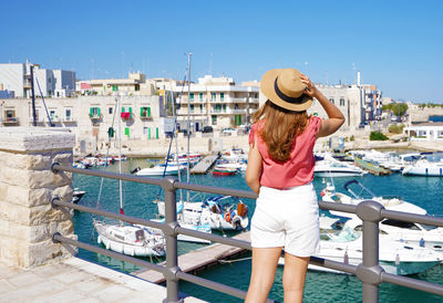 Rear view of woman wearing hat standing at harbor