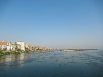 Scenic view of sea by buildings against clear blue sky