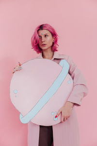 Beautiful young woman holding artificial saturn while standing against colored background