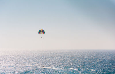 Distant view of person parasailing over sea against clear sky