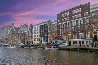 Canal by buildings in city against sky during sunset
