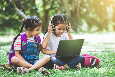 Schoolgirls using laptop while sitting in park