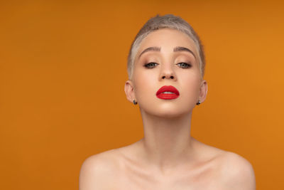 Close-up portrait of young woman against orange background