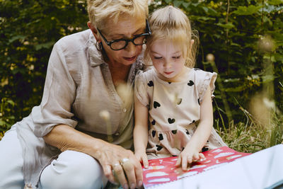 Granddaughter reading book while sitting with grandmother at park