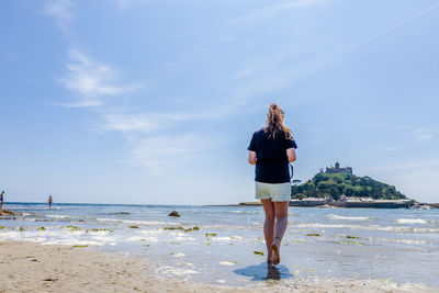 Rear view of woman standing on beach against sky